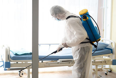 Man in Hazmat protective suits disinfecting in hospital room dur
